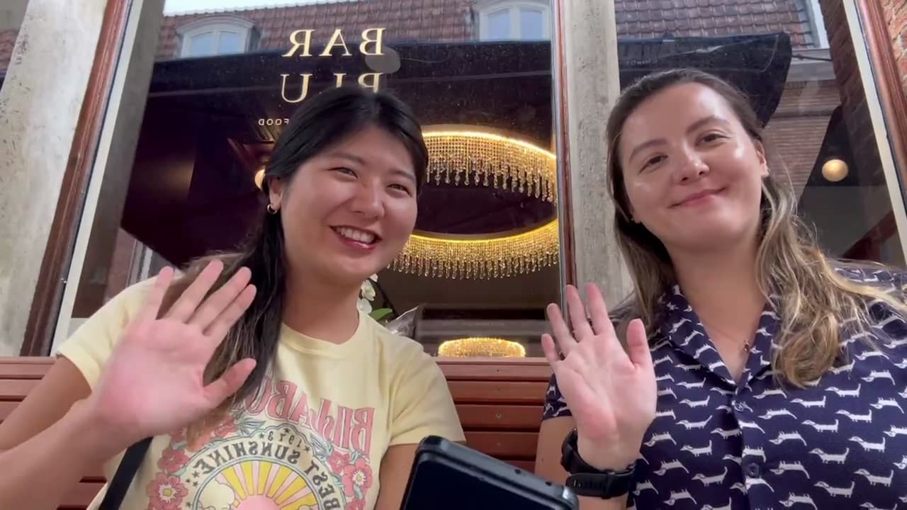 Two people sitting on a bench, one of them waving at the camera